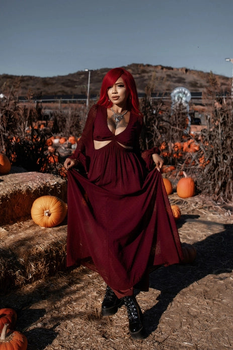 Woman in a burgundy dress standing in a pumpkin patch with hay bales.