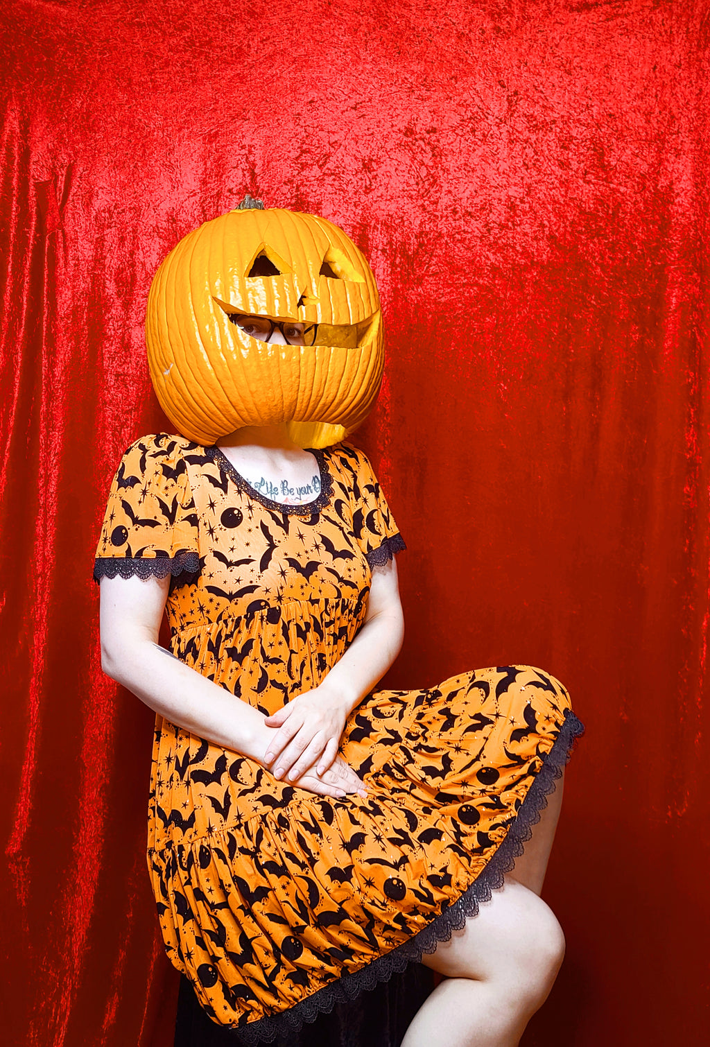 Model wearing a jack-o-lantern head showcasing dress against a red background