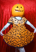 Model wearing a jack o lantern head showcasing dress against a red background