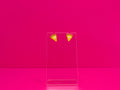 Earrings on a clear display against a hot pink background.