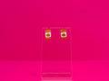 Orange flitter pumpkin spice cup earrings on a clear stand against a pink background.