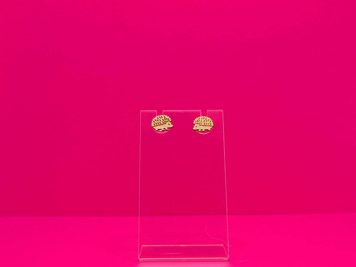 Light brown wood hedgehog earrings against a hot pink background.