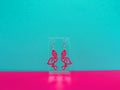Hot pink flamingo earrings against a blue and pink background.