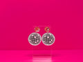 Flat disco ball earrings with a metallic pink topper against a hot pink background.
