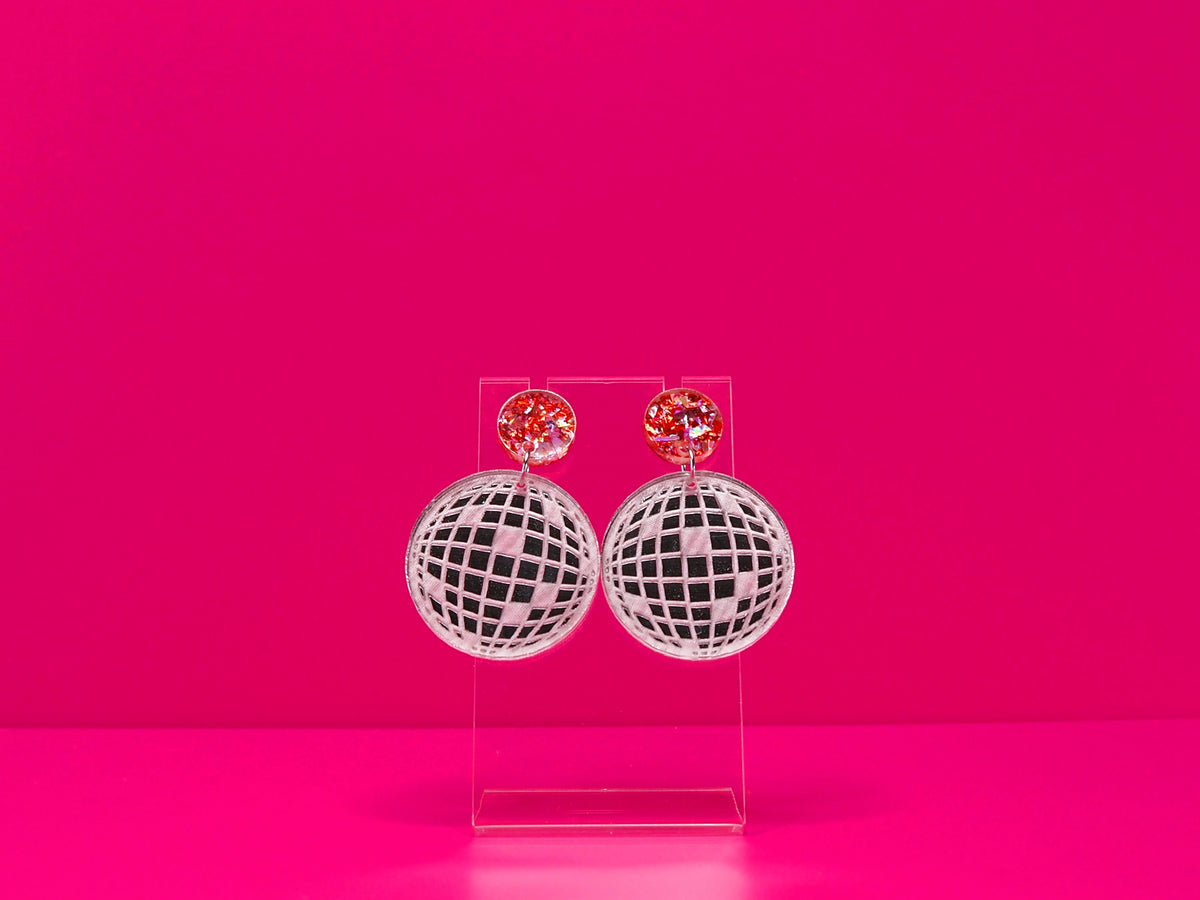Flat disco ball earrings with a metallic pink topper against a hot pink background.