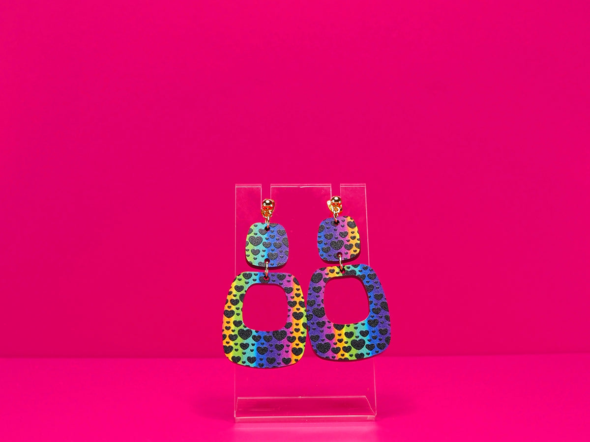Rainbow earrings against a hot pink background.