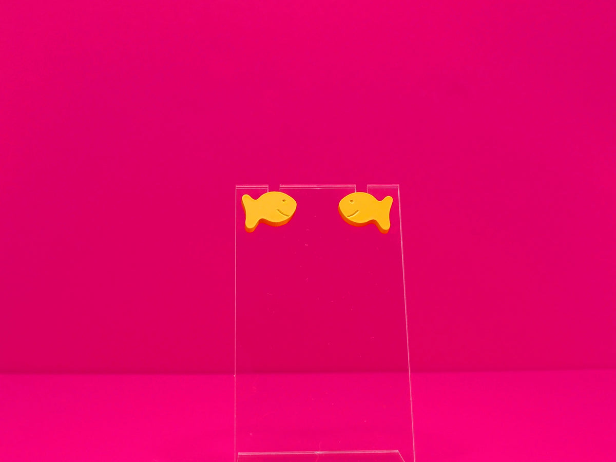 Two orange fish earrings on a clear display against a hot pink background.