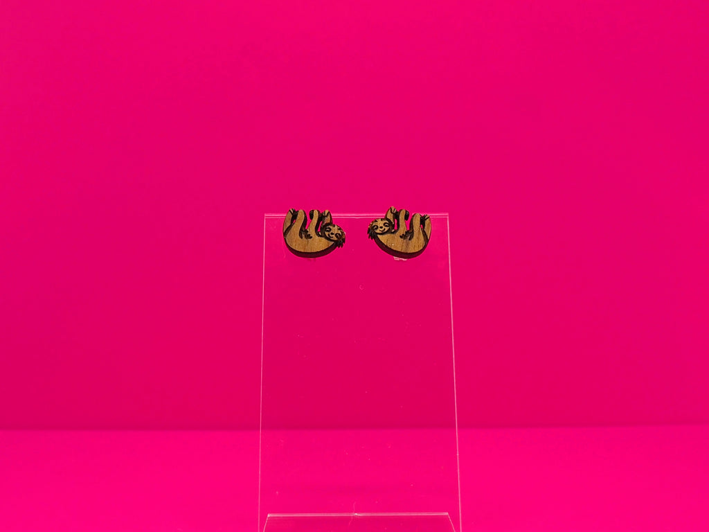 Pair of brown wood sloth earrings on a clear display against a hot pink background.