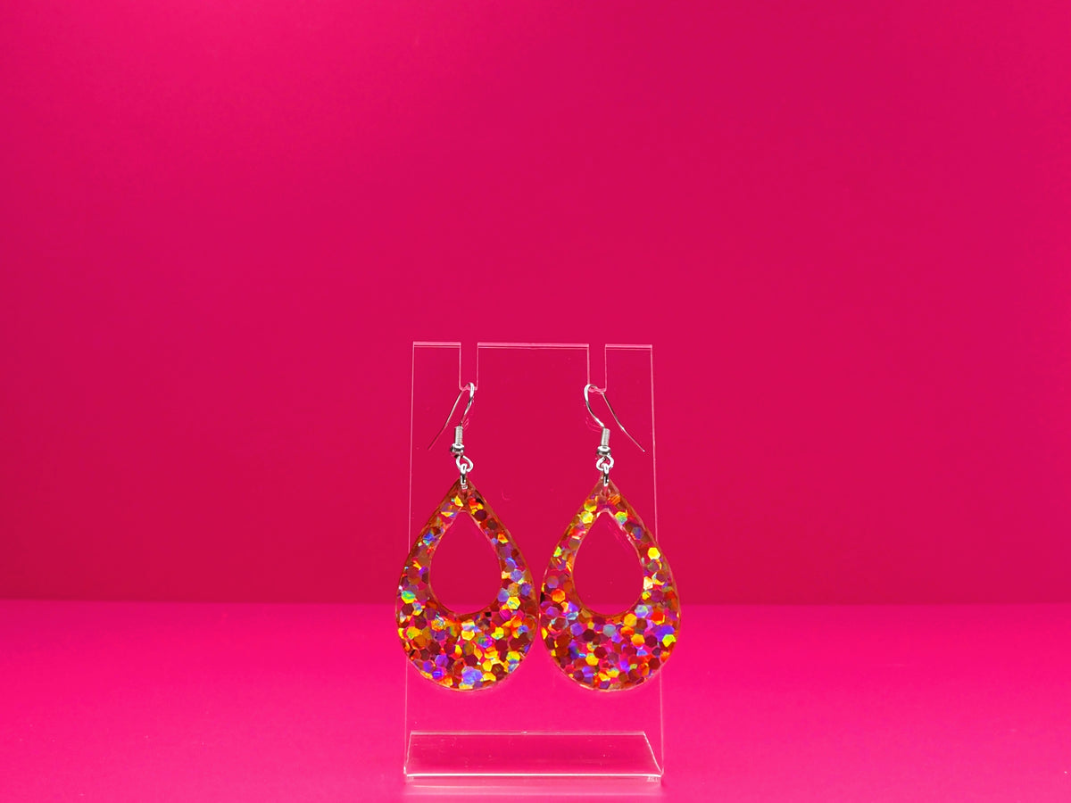 Pink glitter teardrop earrings on a clear display against a pink background.