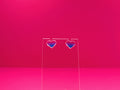 Bisexual pride heart earrings on a clear display against a pink background.