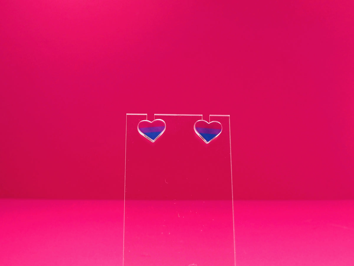 Bisexual pride heart earrings on a clear display against a pink background.