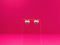 Non-binary pride heart earrings on a clear display against a pink background.