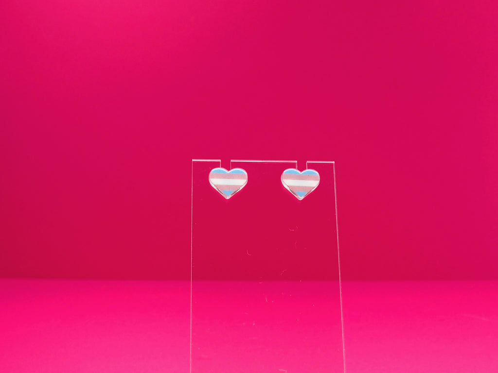 Transexual pride heart earrings on a clear display against a pink background.