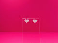 Transexual pride heart earrings on a clear display against a pink background.