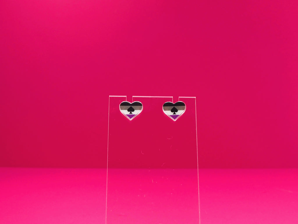 Ace pride heart earrings on a clear display against a pink background.