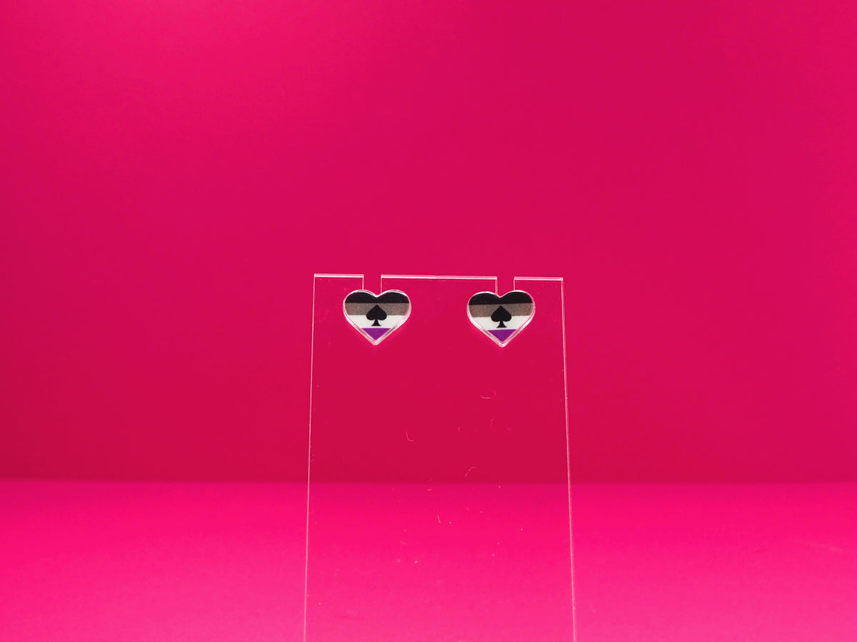 Ace pride heart earrings on a clear display against a pink background.
