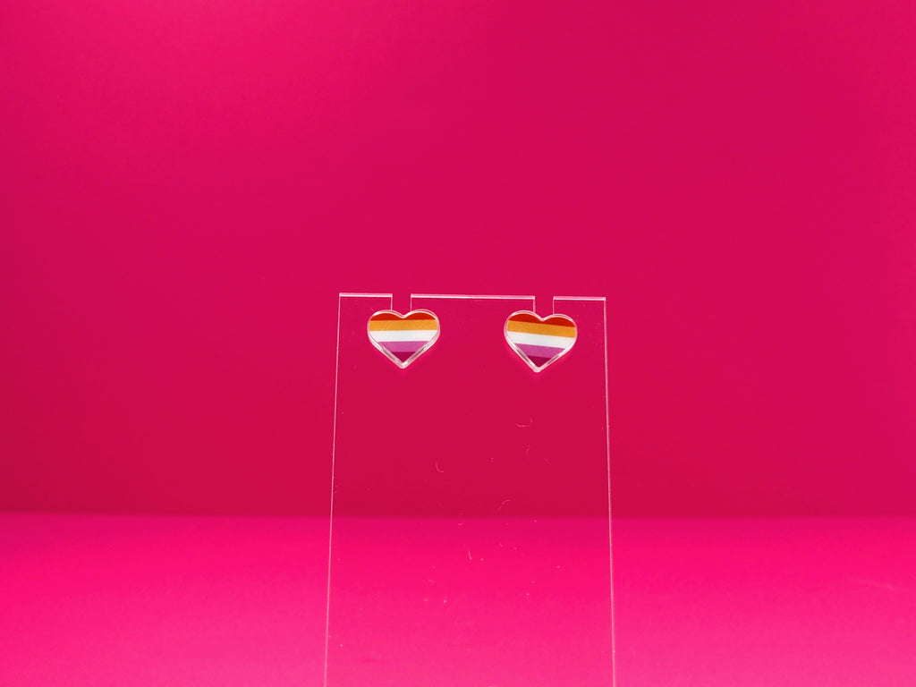 Lesbian pride heart earrings on a clear display against a pink background.