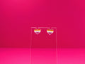 Lesbian pride heart earrings on a clear display against a pink background.