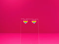 Pansexual pride heart earrings on a clear display against a pink background.