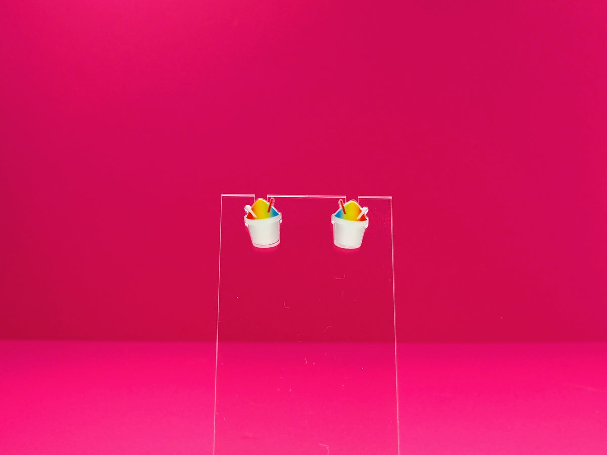 Rainbow snoball earrings on a clear display against a pink background.