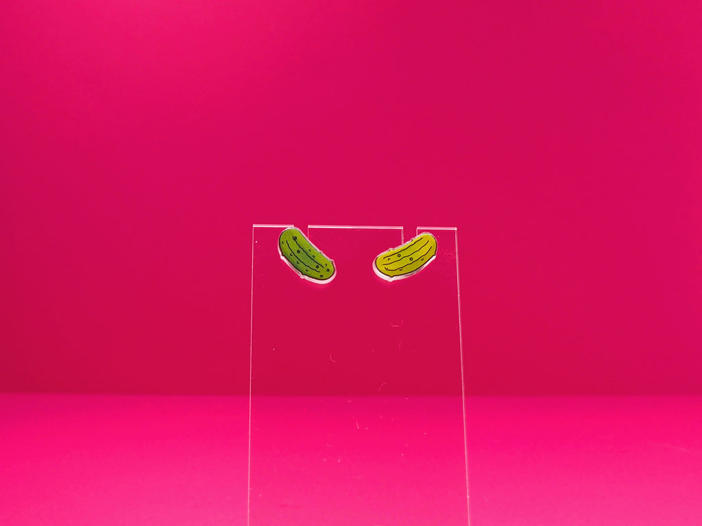Pickle earrings on a clear display against a pink background.