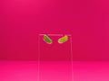 Pickle earrings on a clear display against a pink background.