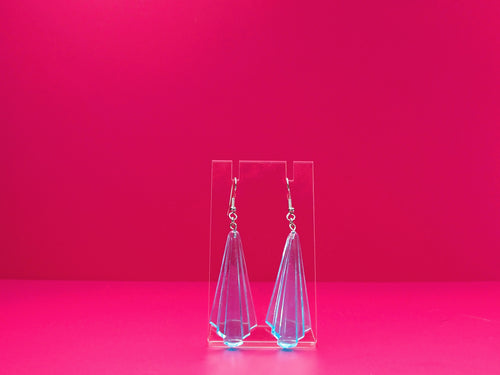 Art deco earrings on a clear display against a pink background.