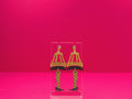 Leg lamp earring on a clear display against a pink background.