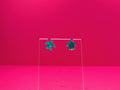 Marbled green sea turtle earrings on a clear display against a pink background.