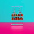 Earrings on a clear stand against a blue and pink background.