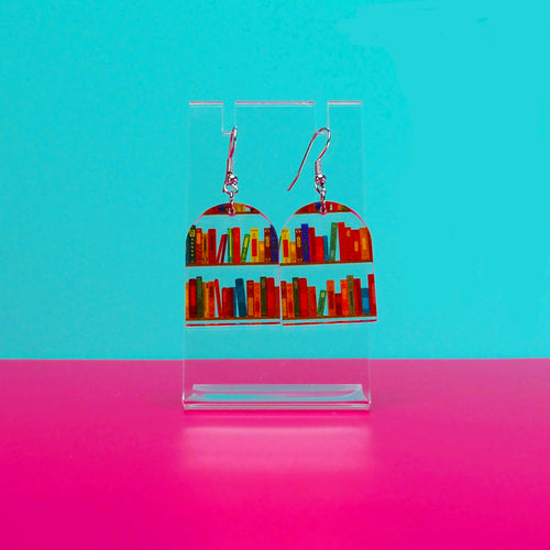 Earrings on a clear stand against a blue and pink background.