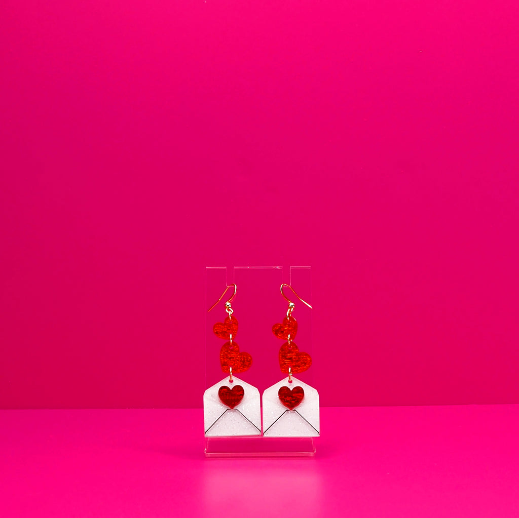 Red hearts cascading into a white envelope on a clear stand against a pink background.