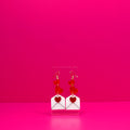 Red hearts cascading into a white envelope on a clear stand against a pink background.