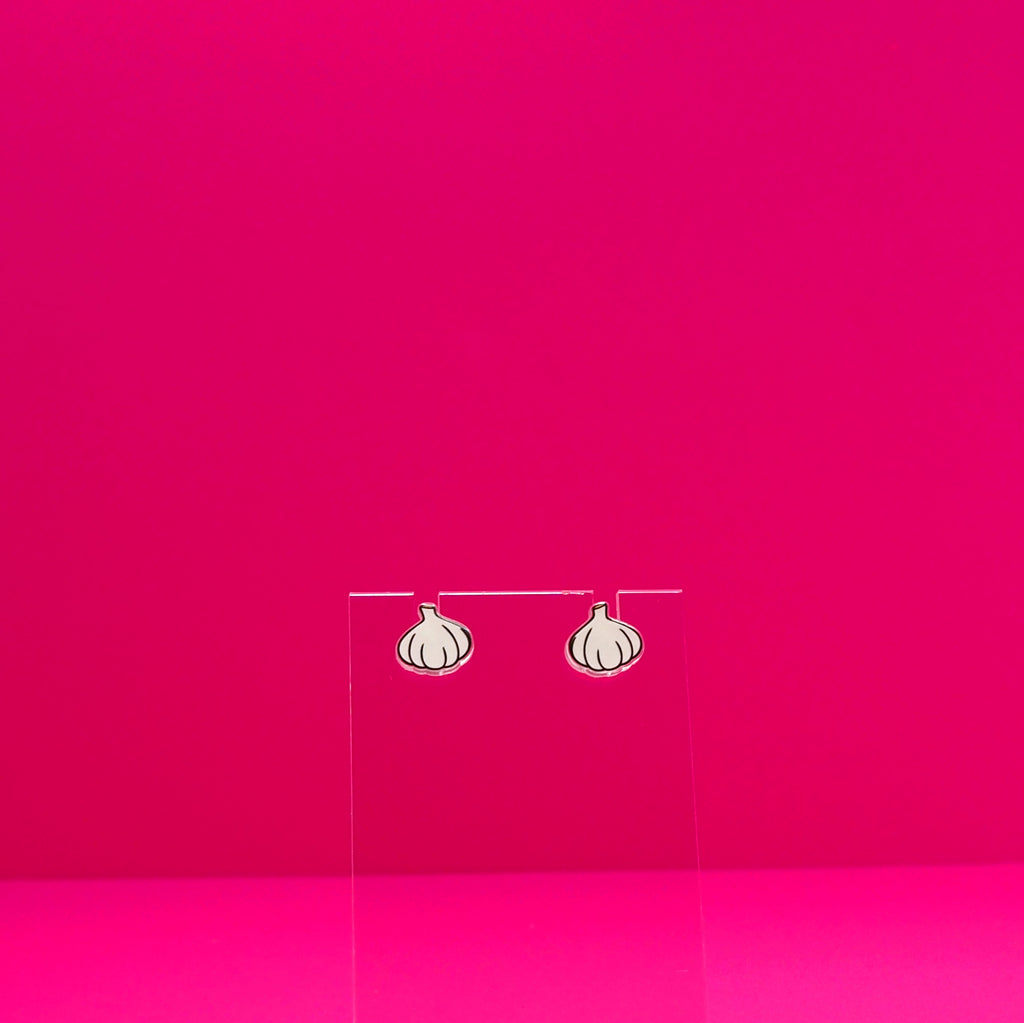 Garlic earrings on a clear stand against a pink background.