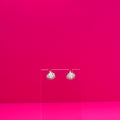 Garlic earrings on a clear stand against a pink background.