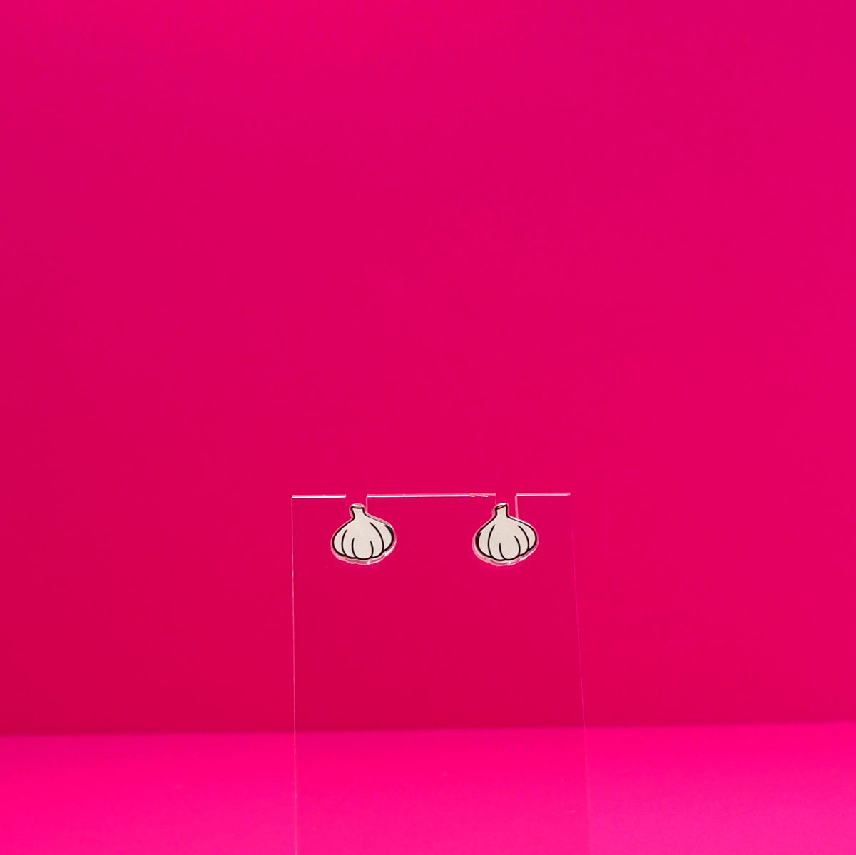 Garlic earrings on a clear stand against a pink background.