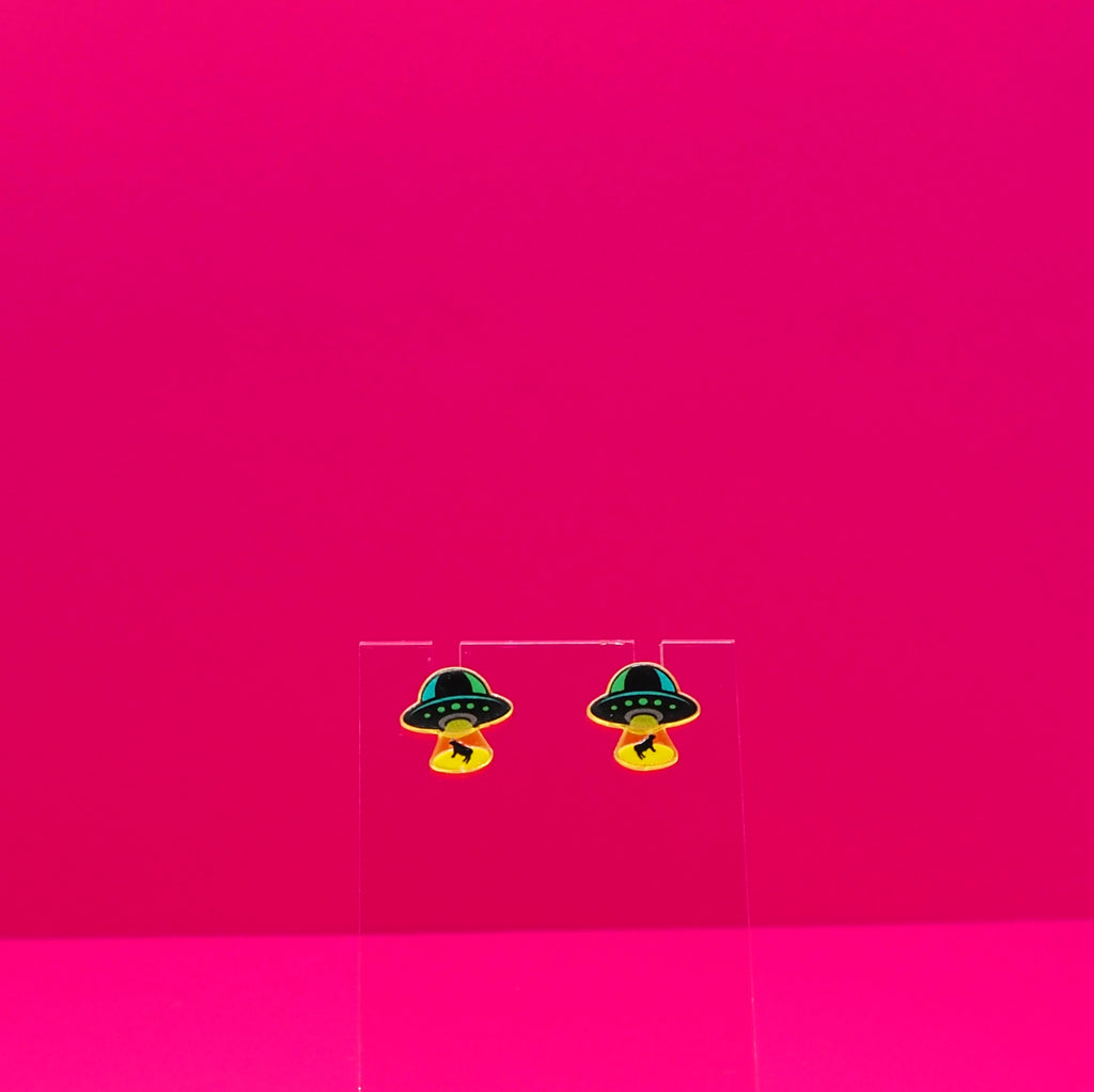 UFO abducting cows on a clear stand against a pink background.