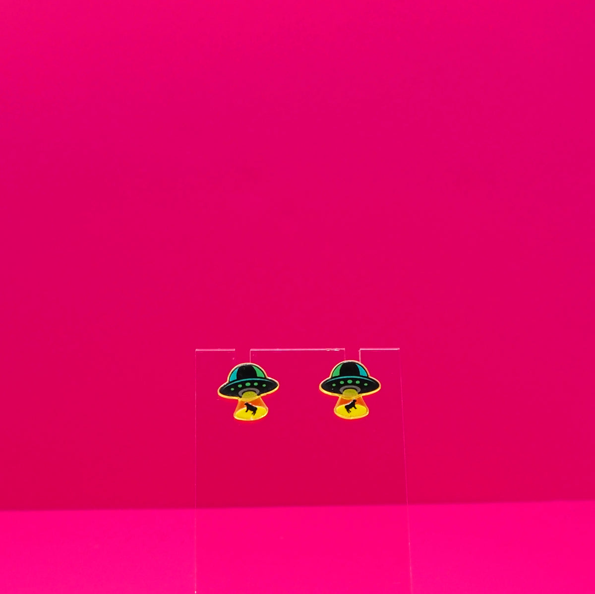 UFO abducting cows on a clear stand against a pink background.