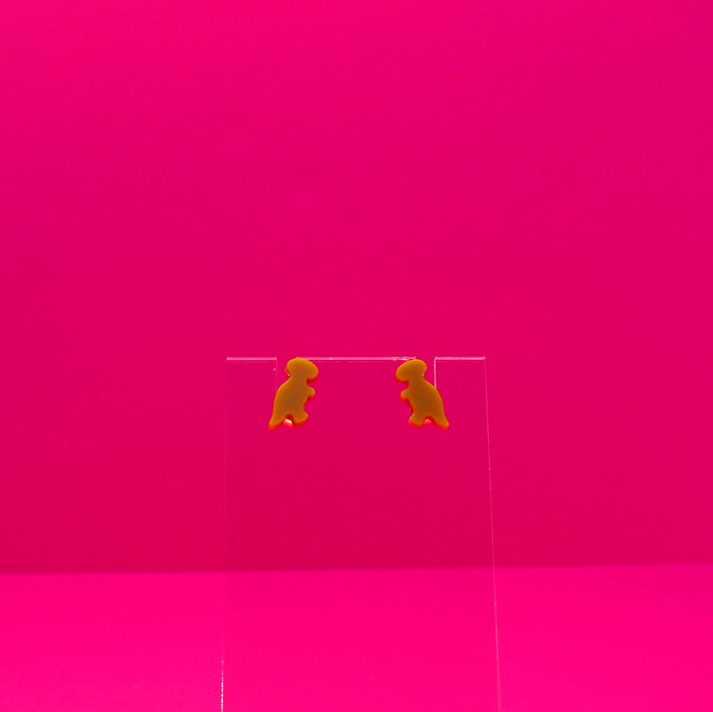 T-Rex earrings on a clear stand against a pink background.