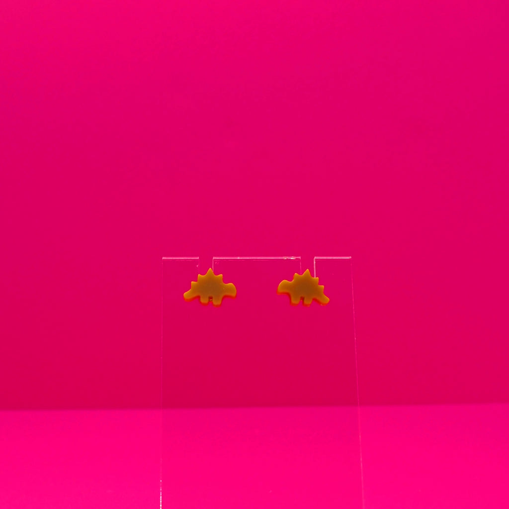 Stegosaurus earrings on a clear stand against a pink background.