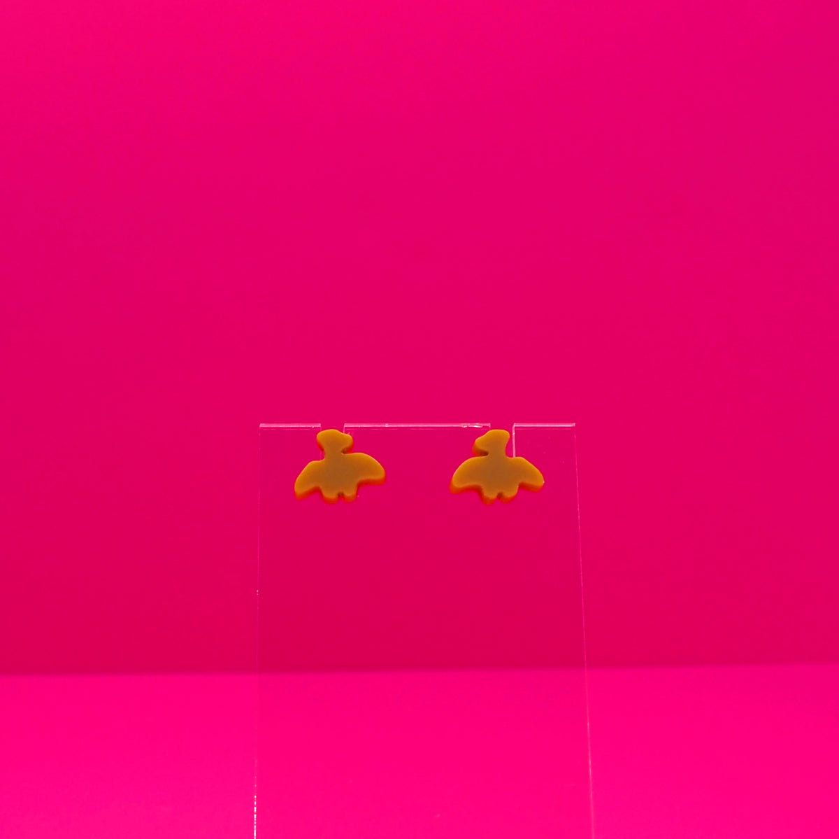 Pterodactyl earrings on a clear stand against a pink background.