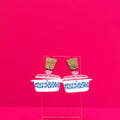 Vintage casserole dish in white earrings with wood accents on a clear display against a pink background.