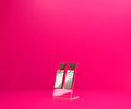 Gold rectangle library card earrings with wood accents on a clear display at an angle against a pink background.