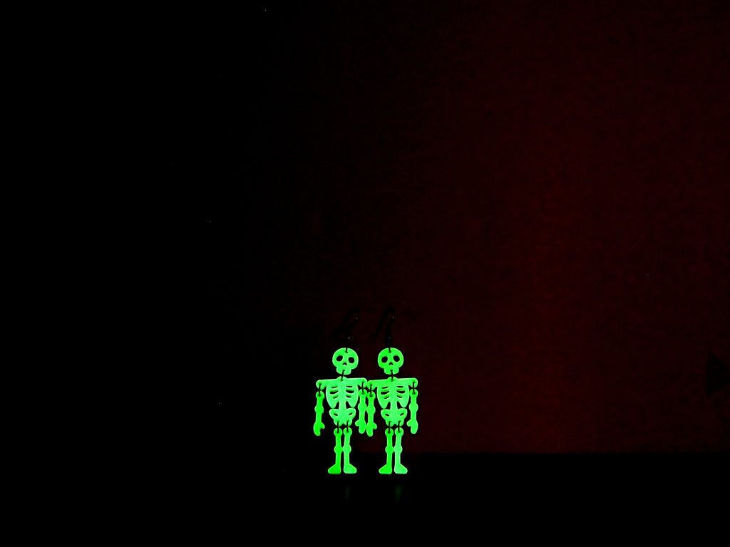Skeleton earrings in the dark to show their green glow against a dark background.