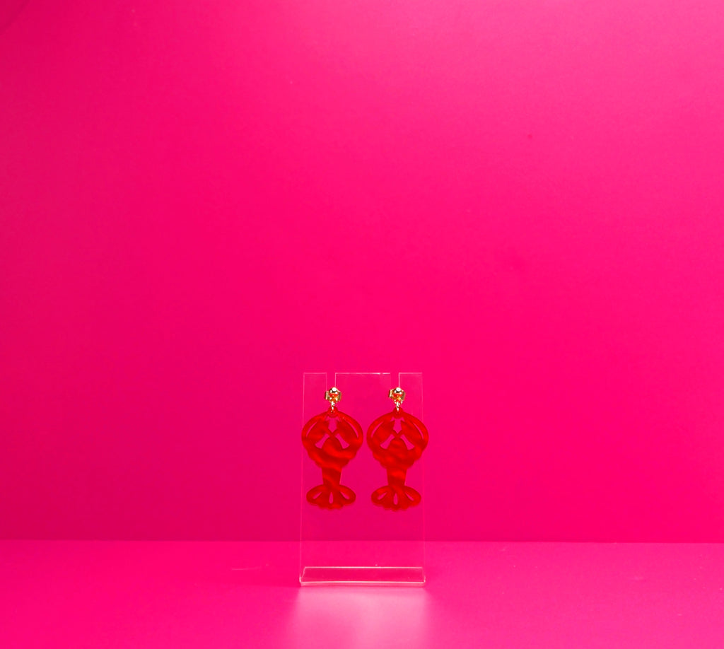 Red marbled lobster earrings on a clear display against a pink background