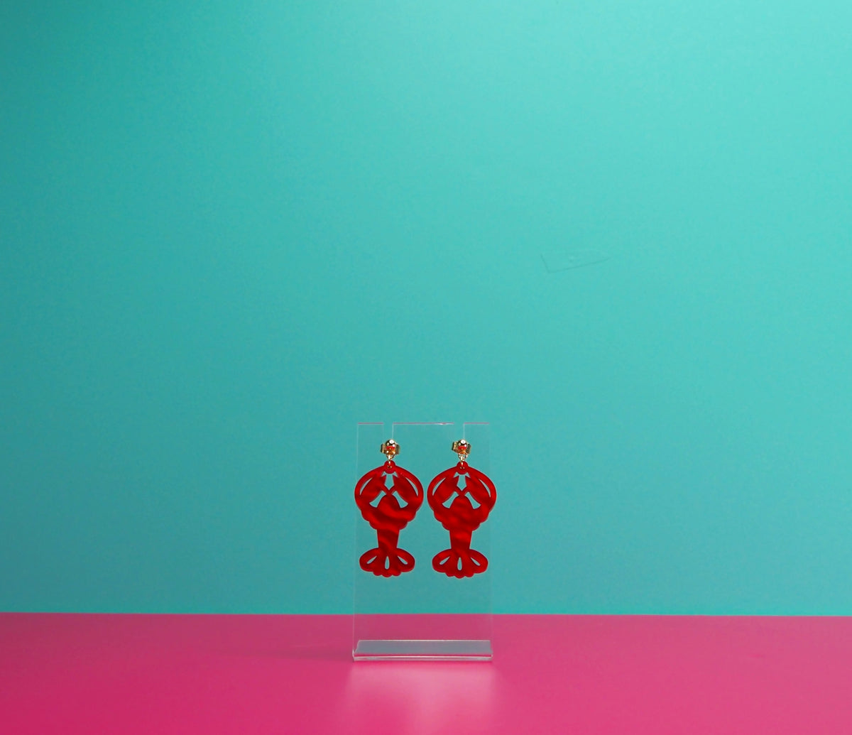Red marbled lobster earrings on a clear display against a blue and pink background.