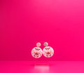 Round pink earrings with moths on a clear display against a pink background.