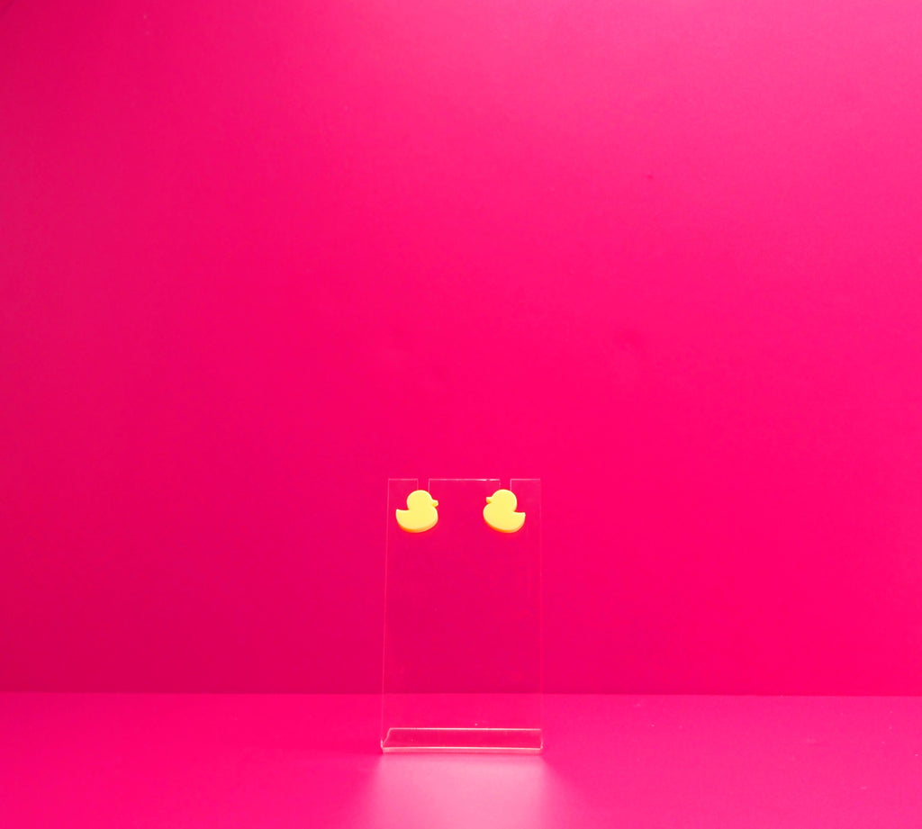 Yellow duck earrings on a clear display against a pink background.