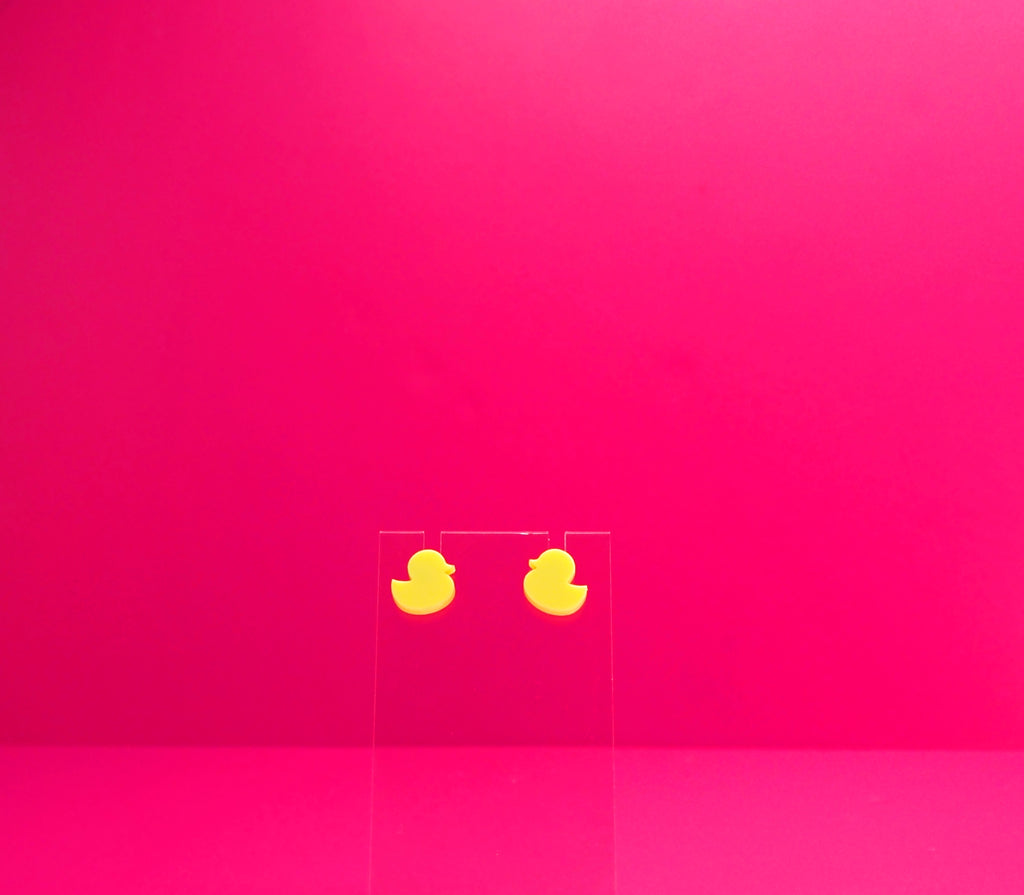 Yellow duck earrings on a clear display against a pink background.