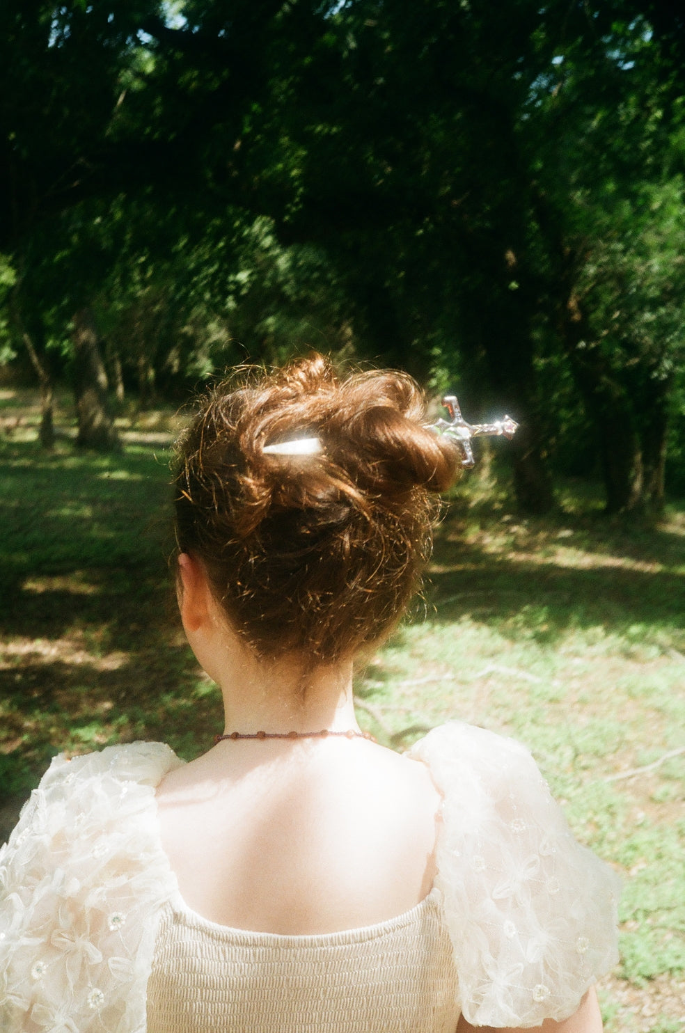 Brunette model with hair sword in their bun against a bright wooded background.